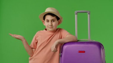 Mor bavulun yanında duran şapkalı genç çocuk avucunun içine bakıyor, fotokopi odası. Krom anahtar yeşil ekran yeşil ekran stüdyo arka plan modelinde izole edilmiş. Yavaş çekim