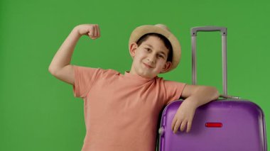 Mor bavulun yanında duran şapkalı genç çocuk kollarını göstermekten mutluluk duyuyordu. Krom anahtar yeşil ekran yeşil ekran stüdyo arka plan modelinde izole edilmiş. Yavaş çekim