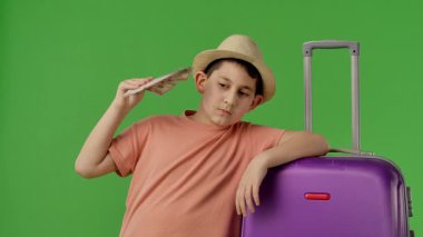 Mor bavulun yanında duran genç bir çocuk ve elinde dolarların hayranı var. Krom anahtar yeşil ekran yeşil ekran stüdyo arka plan modelinde izole edilmiş. Yavaş çekim