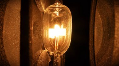 Kaba desenli yüzeylerle çevrili parlayan bir halojen ampulün yakın görüntüsü. Sıcak aydınlatma ve detaylı dokular dramatik ve endüstriyel bir estetik yaratıyor..