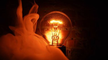 Tungsten ampul lambası siyah arka planda dalgalı dumanla birlikte. Aydınlık ve karanlık kavramı, fikir, elektrik modern evde.