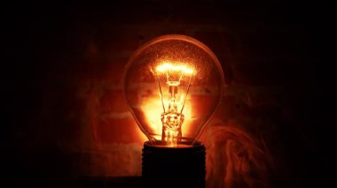 Tungsten ampul lambası siyah arka planda dalgalı dumanla birlikte. Aydınlık ve karanlık kavramı, fikir, elektrik modern evde.