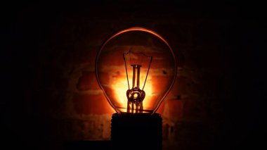 Tungsten lambası, karanlıkta tuğla duvara karşı. Aydınlık ve karanlık kavram, fikir, evde elektrik. Retro fikir.
