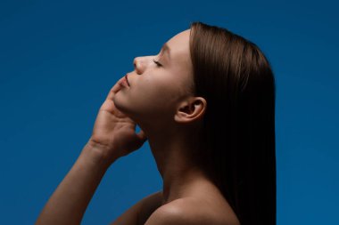 Yan profilde gözleri kapalı ve elleri çenesinde mavi arka planı olan bir kadın var..