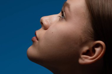 Koyu mavi arka planda bir kadının yakın plan profili. Görüntü kadınların sakin ifadesine ve pürüzsüz cildine odaklanıyor..