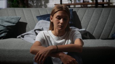 Genç bir birey koltukta oturur, derin düşüncelere dalmış ya da derin düşüncelere dalmış bir şekilde, sakin ama içsel bir atmosfer yaratır..