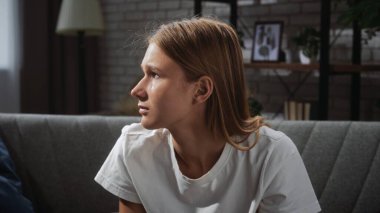 Genç bir kadın kanepede oturur, düşünceli ve düşünceli bir şekilde ev ortamında..