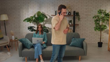 Telefonda konuşan bir adam ve şık bir oturma odasında dizüstü bilgisayar kullanan bir kadın..