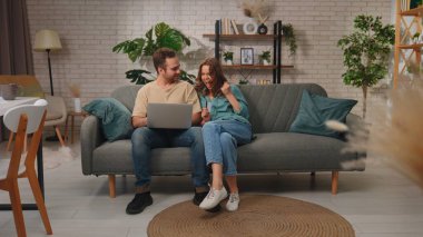 Neşeli bir çift kanepelerinde oturmuş, bir dizüstü bilgisayar ve kredi kartı kullanarak başarılı bir online alışveriş yapmayı kutluyorlar..