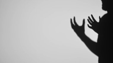 Gölgeli bir el silueti, el kol hareketi yapıyor ya da düz, aydınlık bir zemine uzanıyor gibi görünüyor..