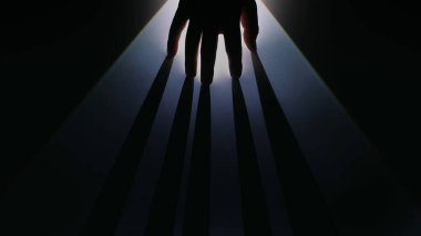 Siluetli bir el, loş ışıkta dramatik gölgeler bırakır, gizem ve yaratıcılık uyandırır..