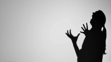 Elleri havada, duyguları minimalist siyah-beyaz bir şekilde aktaran bir kişinin dramatik gölgesi..