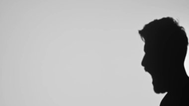 Işık arka planına karşı bağıran bir adamın yan profil silueti öfke ya da hayal kırıklığını simgeler..