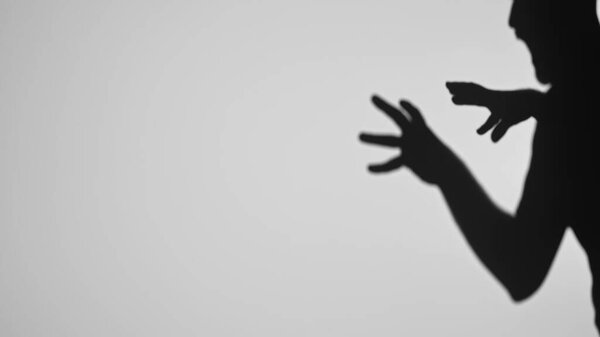 Photograph of a persons shadow forming an intriguing silhouette with outstretched hands on a light background.