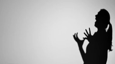 Elleri havada, duyguları minimalist siyah-beyaz bir şekilde aktaran bir kişinin dramatik gölgesi. Yavaş çekim