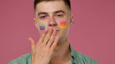 Gökkuşağı suratlı bir adam pembe bir arka plana öpücük yolluyor. Gurur ve kabulü simgeliyor..