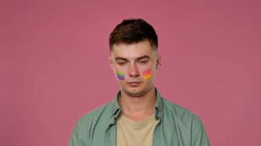 Pembe arka planda yüzü gökkuşağı gibi olan genç bir adam başını eğip kameraya bakıyor ve LGBT gururunu ve kimliğini simgeliyor..