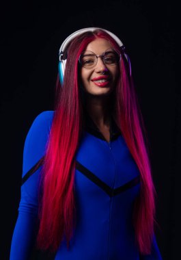 Pembe saçlı, mavi fütüristik bir kıyafet, gözlük ve kulaklık takan şık bir kadın. Karanlık bir arka plana karşı güvenle gülümsüyor..