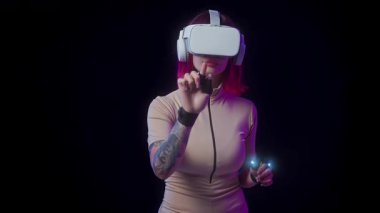 Pembe saçlı, sanal gerçeklik kulaklığı takan ve sanal bir arayüzle etkileşimde olan akıllı eldivenli bir kadın. Siyah arkaplan fütürist teknoloji kavramını vurguluyor.