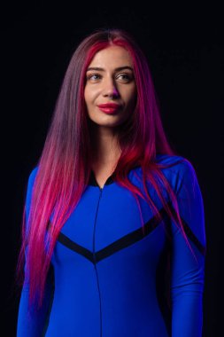 Uzun düz pembe saçlı bir kadının portresi. Üzerinde siyah detaylar olan modern mavi bir beden giyiyor. Esmer arka planda, neon ışıklı bir şekilde poz veriyor. Fütürist moda ve siber punk estetiği.