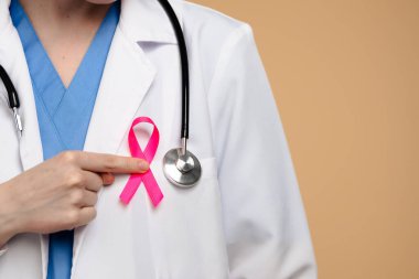 Steteskop ve pembe kurdeleli beyaz önlüklü doktor, farkındalığın sembolü olarak kurdeleyi işaret ediyor. Göğüs kanseri farkındalık günü konsepti.