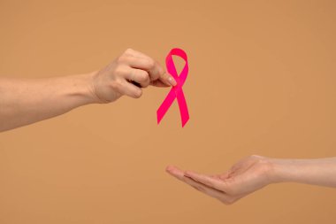 Göğüs kanseri farkındalığını ve desteğini simgeleyen pembe kurdele takan iki el. Kadın dayanışması ve desteği.