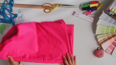 Pembe kumaşın bir kısmını ütüleyen terzi ellerinin üst görüntüsü. Yaratıcı projeler için kumaş, makas ve iplik içeren bir dikiş malzemesi koleksiyonu. Atıcı, terzilik ve giysi tasarımı konsepti.