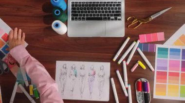 Tasarımcıların masasındaki temizlik işleminin zamanı. Kadın düzgün bir şekilde elbise taslakları, paletler, iplikler, renkli keçeli kalemler ve makaslar veriyor. Atıcı, tasarım konsepti. Üst görünüm.