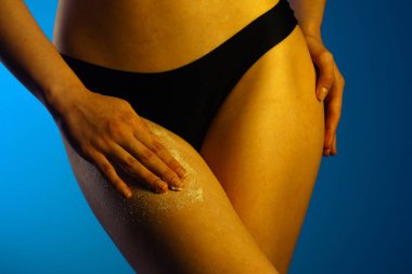 Kadın bacağına deri dökücü krem süren, cilt bakımını ve cilt bakımını ön plana çıkaran bir elin yakın plan resmi..