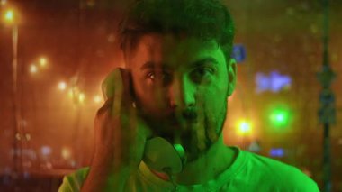 Telefon kulübesinde sakallı, yeşil ve kırmızı ışıklı bir adam. Ön planda damlayan yağmur damlaları, arka planda şehrin bulanık ışıkları. Retro kavramı.