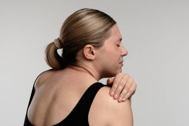 Bir kadın omzunu tutarken tasvir edilir, muhtemelen rahatsızlık ya da acı hisseder. Sağlık, tedavi ve ağrı kesici kavramı.