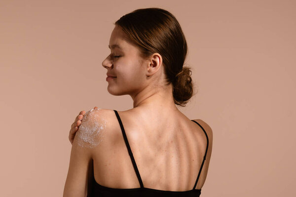 Женщина нежно наносит средство для ухода за кожей на плечо, стимулируя здоровую и увлажненную кожу.