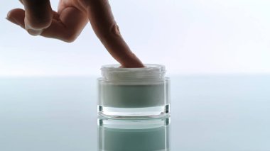 Bir elin, dokuyu ve saflığı vurgulayan cilt kremi kavanozuna parmağını daldırdığı yakın plan görüntüsü..