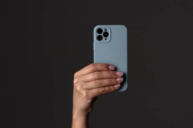 Mavi bir çantada modern bir akıllı telefonu tutan bir el, karanlık bir arkaplanda kamera tasarımını ön plana çıkarıyor..