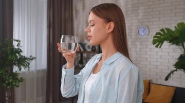 Genç bir kadın evde bir bardak temiz su içerek susuzluğun ve sağlıklı bir yaşam tarzının önemini vurgular..