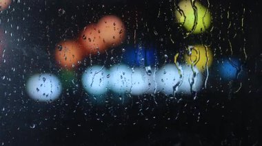 Geceleri arka planda bulanık şehir ışıkları olan pencere camına yağmur damlaları. Canlı bir bokeh etkisi rüya gibi bir şehir atmosferi yaratır..