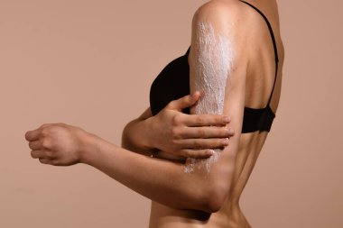 Bir kadın, cilt bakımı için koluna kabuk bağlıyor. Arka plan yumuşak, nötr bir renktir..