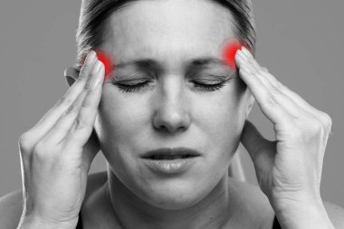 Bir kadın şakaklarını tutarken görülüyor. Ağrıyı ya da rahatsızlığı gösteriyor. Baş ağrısı ya da stresiyle ilgili olabilir. Sağlık, tedavi ve ağrı kesici kavramı.
