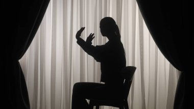 Sandalyede oturan ve dur işareti yapan bir kadının silueti. Perdeleri olan yumuşak ışıklı bir pencerenin önündeki kadın hayal kırıklığını, stresi ve depresyonu ifade ediyor. Ruh sağlığı konsepti.