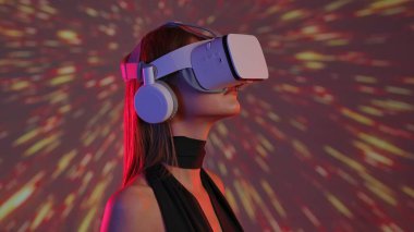 Sanal gerçeklik kulaklığı takan bir kadın kendini renkli soyut aydınlatma efektleriyle dijital bir deneyime sokuyor. Dijital sanat görselleştirmesi için bir alan, geleceğin teknolojisi..
