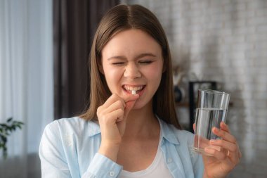 Genç bir kadın evde ilaç almaya hazırlanan bir hap ve bir bardak su tutuyor. Sağlıklı yaşam konsepti, cilt ve saç için vitamin almak..