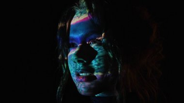 Renkli ışık desenleriyle aydınlanan bir kadın karanlık bir arkaplan karşısında canlı ve gerçeküstü bir görsel efekt yaratır..