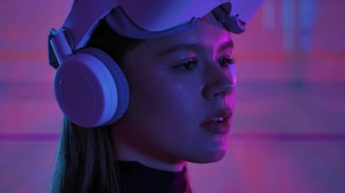 Sanal gerçeklik kulaklığı takan bir kadın kendini renkli soyut aydınlatma efektleriyle dijital bir deneyime sokuyor. Dijital sanat görselleştirmesi için bir alan, geleceğin teknolojisi..