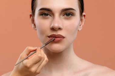 Güzellik tekniklerini vurgulayarak, bir kadının yüzüne dudak makyajının titiz bir şekilde uygulanmasını gösteren yakın plan bir resim..