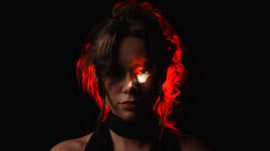 Parlak kırmızı ışıkla aydınlatılmış, yüzünde ateş yansıması olan bir kadının dramatik portresi gergin ve gizemli bir atmosfer yaratıyor..