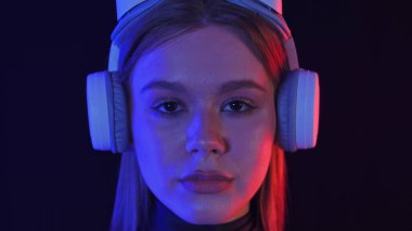 VR kulaklık takan bir kadın karanlık bir ortamda sanal gerçekliği keşfediyor. Sahne mavi ve kırmızı ışıkla aydınlatılıyor, gelecekteki deneyimi vurguluyor..