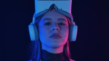 VR kulaklık takan bir kadın karanlık bir ortamda sanal gerçekliği keşfediyor. Sahne mavi ve kırmızı ışıkla aydınlatılıyor, gelecekteki deneyimi vurguluyor..
