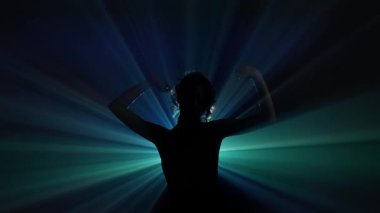 Karanlık bir arkaplana poz veren gizemli bir kadın silueti. Etrafı dramatik mavi ve deniz mavisi ışıklarıyla çevrili. Işıl ışıl, sinematik bir hale oluşturuyorlar. Yavaş çekim.