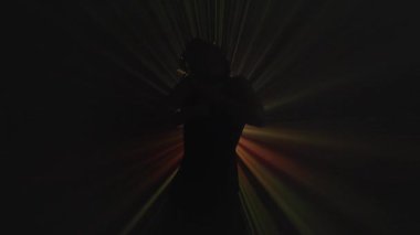 Keskin altın ışıklarla vurgulanmış, siyah bir alanda gizemli ve dramatik bir görüntü oluşturan bir kişinin karanlık silüeti. Yavaş çekim.