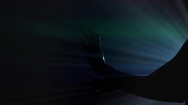 Bir kadının dramatik bir silueti canlı bir gökkuşağı ışık projeksiyonuna karşı duruyor, gizemli, sanatsal bir kompozisyonda vücudunun ana hatlarını belirten parlak bir renk patlaması yaratıyor. Yan görüş. Yavaş çekim.